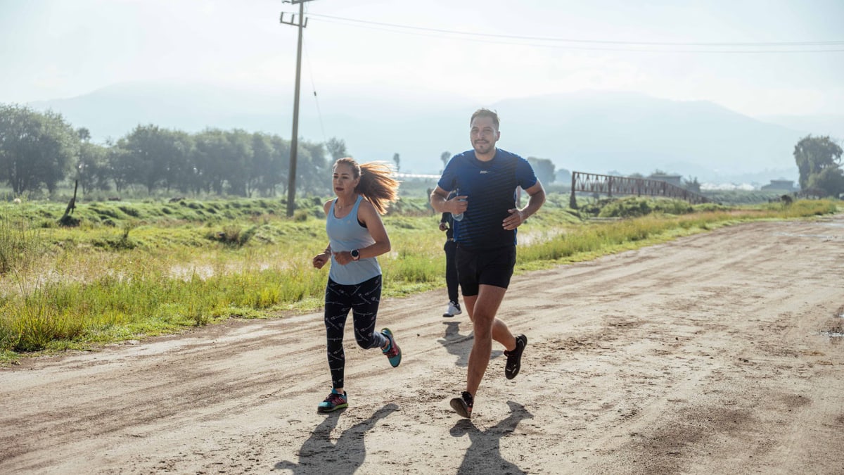Group of joggers running along a rural dirt path surrounded by nature.